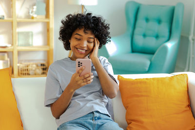 Young woman using phone while sitting on sofa at home