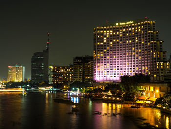 Illuminated buildings by river against sky at night