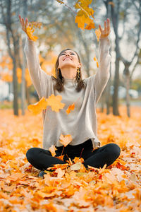 Portrait of young woman with arms raised standing on field