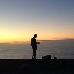 Silhouette man standing on beach against sky during sunset