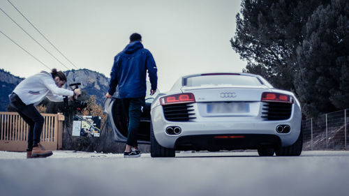 Rear view of people standing on car against sky