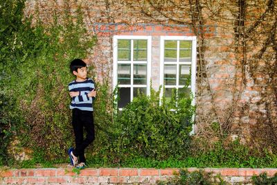 Thoughtful boy with arms crossed standing against ivy wall