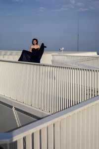 Woman sitting on railing against sky