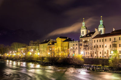 Illuminated buildings by canal against sky at night