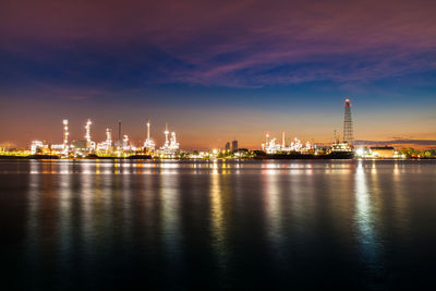 Illuminated city at waterfront during sunset