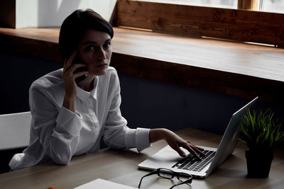 Young woman using mobile phone while sitting on table