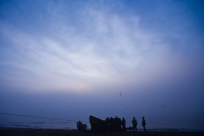 Silhouette people on beach against sky during sunset