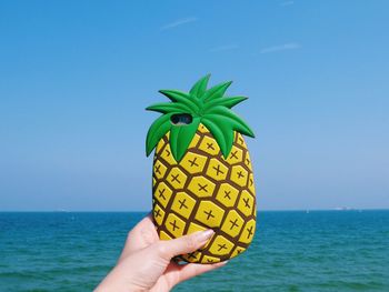 Close-up of hand holding smart phone with pineapple shaped cover by sea
