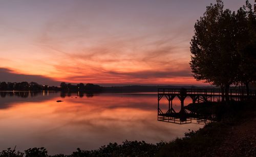 Silhouette trees by lake against sky during sunset