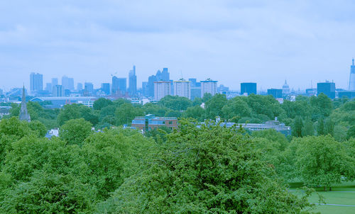 Trees and buildings in city against sky