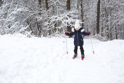 Children's feet in red plastic skis with sticks go through the snow from a 