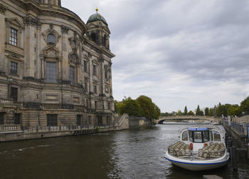 View of buildings by river against cloudy sky