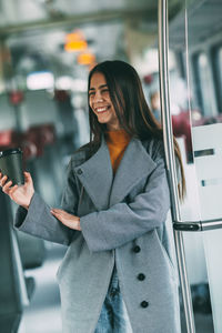 Woman holding smart phone while standing on laptop