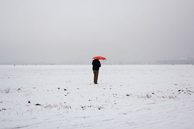 Person with umbrella standing on snow covered landscape against sky