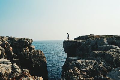 Rear view of man standing on rock by sea against clear sky