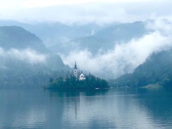 Scenic view of lake bled against mountains during foggy weather
