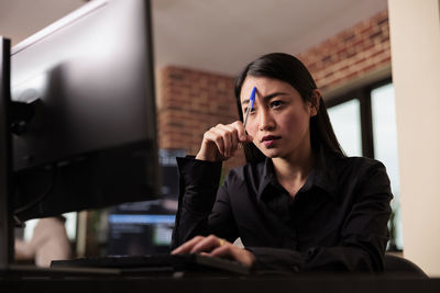 Portrait of young woman using mobile phone while sitting in office