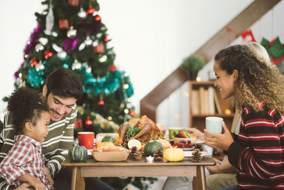 People sitting by food on table against christmas tree