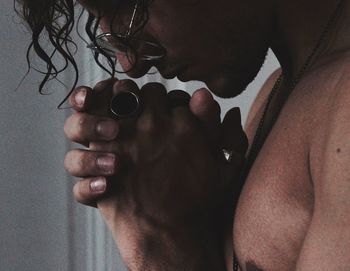 Midsection of shirtless young man praying by wall