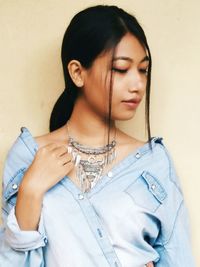 Young woman wearing necklace while standing against wall