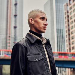 Man looking away while standing against buildings in city