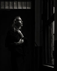 Young woman looking through window in dark