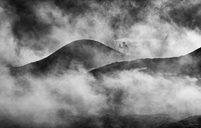 Person climbing on mountain against sky during foggy weather