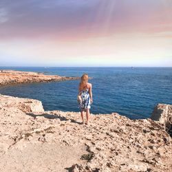 Full length of young woman standing on beach against clear sky