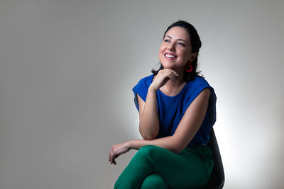 Portrait of smiling young woman sitting against gray background