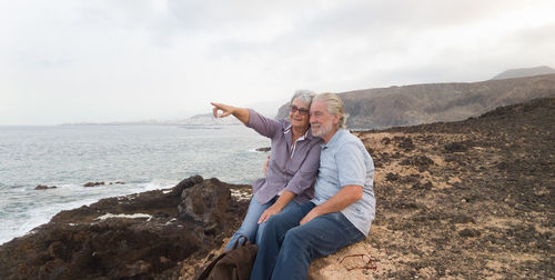 People sitting on rock by sea against sky