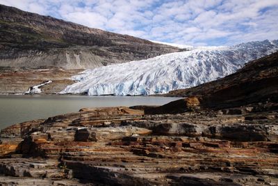 Glaciers at riverbank by mountain against sky