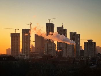 Smoke coming out from factory against buildings in city at sunset