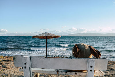 Teddy bear on bench at beach against blue sky during sunny day