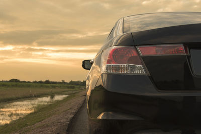 Car on road by field against sky during sunset