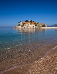 Scenic view of sea by buildings against clear blue sky