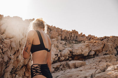 Rear view of woman standing on rock against clear sky