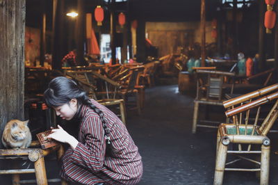 Side view of woman crouching by cat on table at restaurant