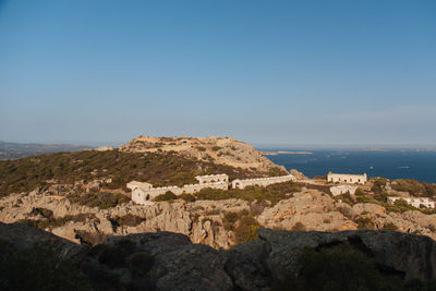 Scenic view of rocks by sea against clear blue sky