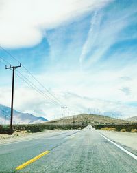 Road by electricity pylons against sky
