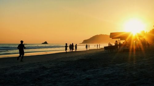 Silhouette people on beach against sky during sunset