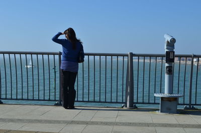 Rear view of woman standing on railing against sea