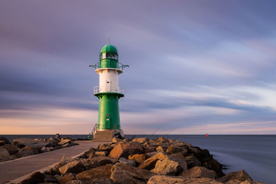 Lighthouse on rock by sea against sky