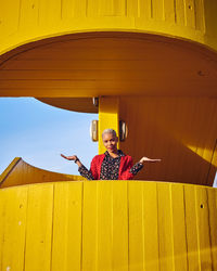 Portrait of smiling woman sitting against yellow wall