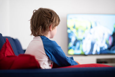 Rear view of little boy sitting on a sofa watching tv