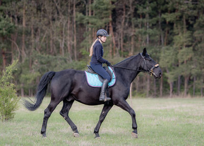 Woman riding horse against trees on field