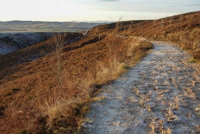 Dirt road amidst land against sky