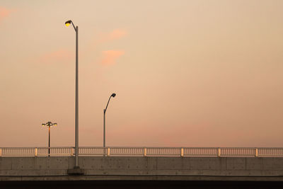 Street lights by sea against sky during sunset