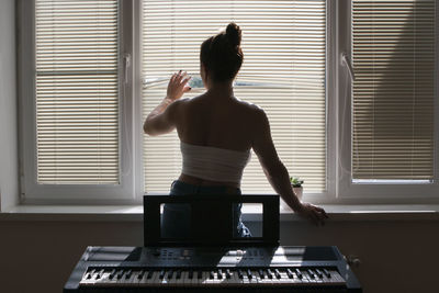 Young woman musician standing at the window. view from behind.