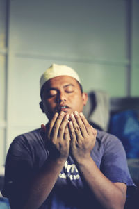 Man praying against wall at home