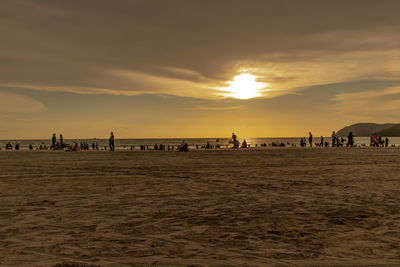 People on beach against sky during sunset